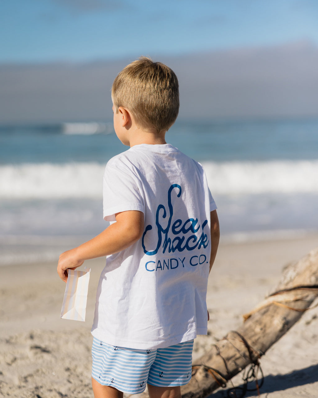 Child wearing a 'Sea Shack Candy Co.' shirt on a beach