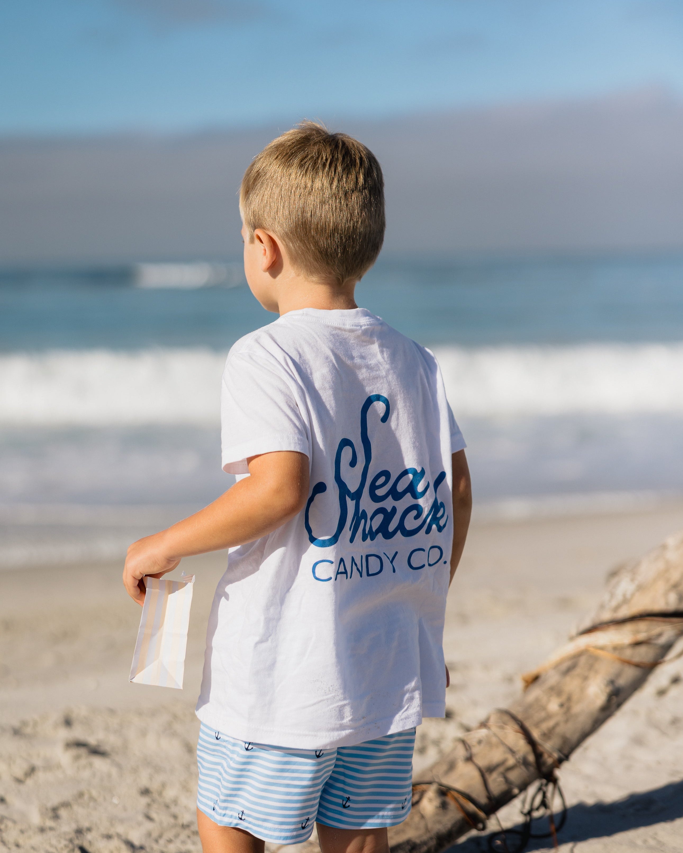 Child wearing a 'Sea Shack Candy Co.' shirt on a beach